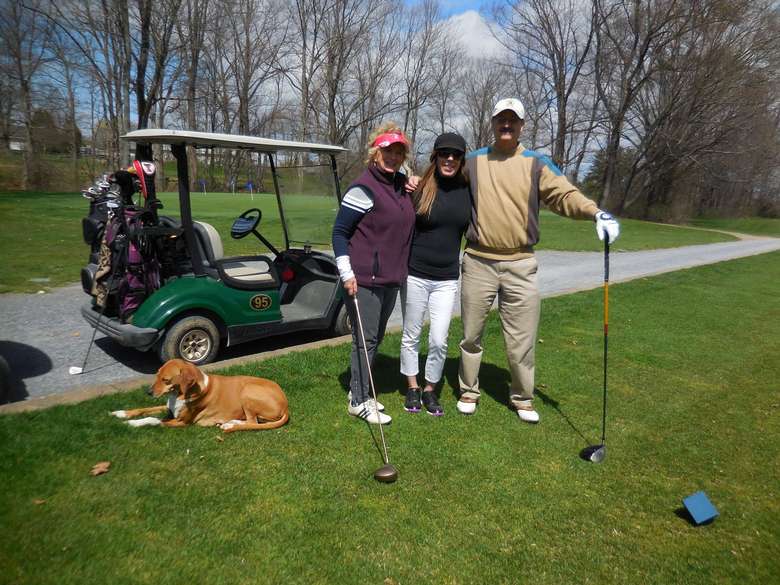 three golfers and their dog posing in front of a golf cart