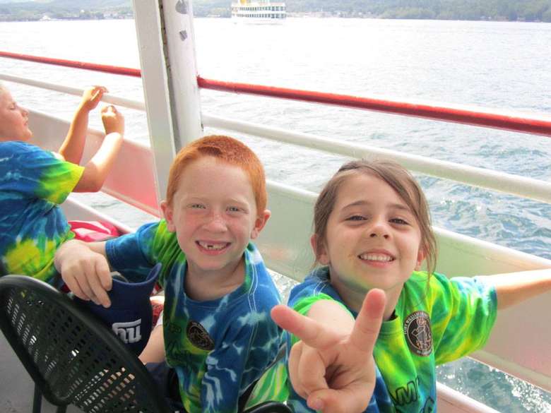 two kids in a boat, one giving the peace sign
