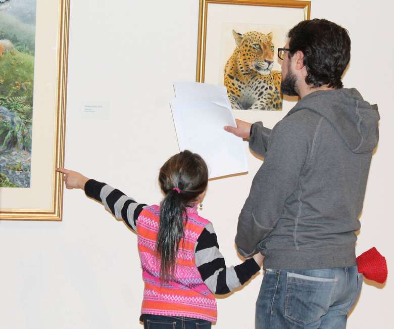 a man holding a piece of paper near artworks, a girl is near him