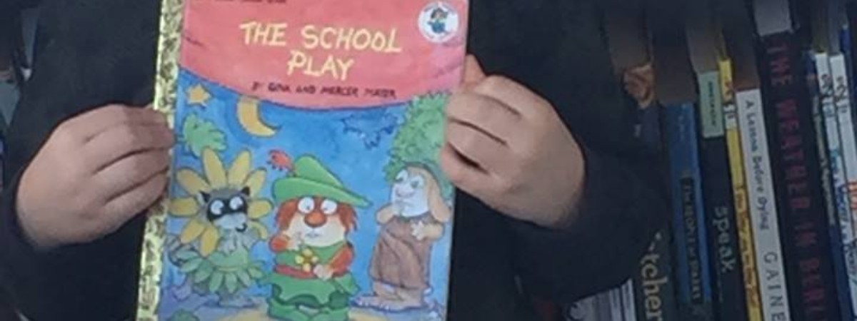little boy in front of bookshelf holding up a book