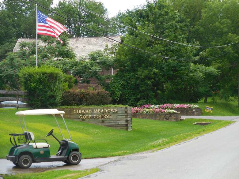 front entrance of airway meadows with a golf cart and an american flag