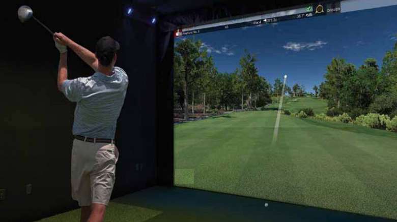 man swinging golf club facing a golf simulator screen