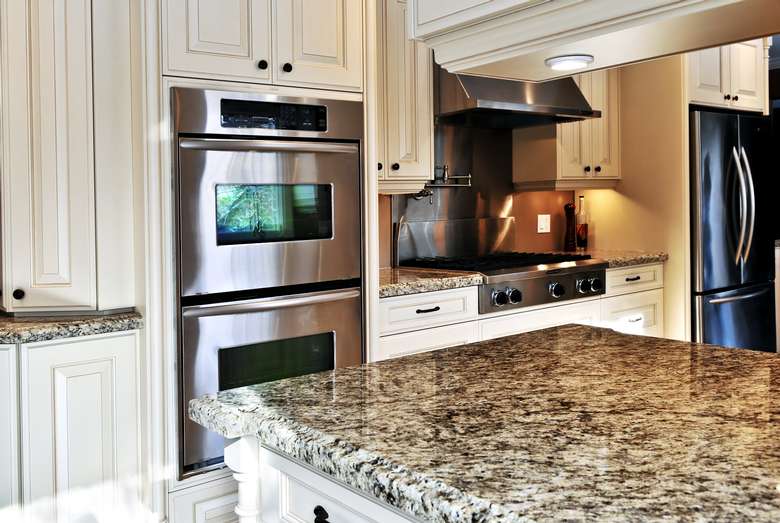 a kitchen with white cabinets, marble countertop