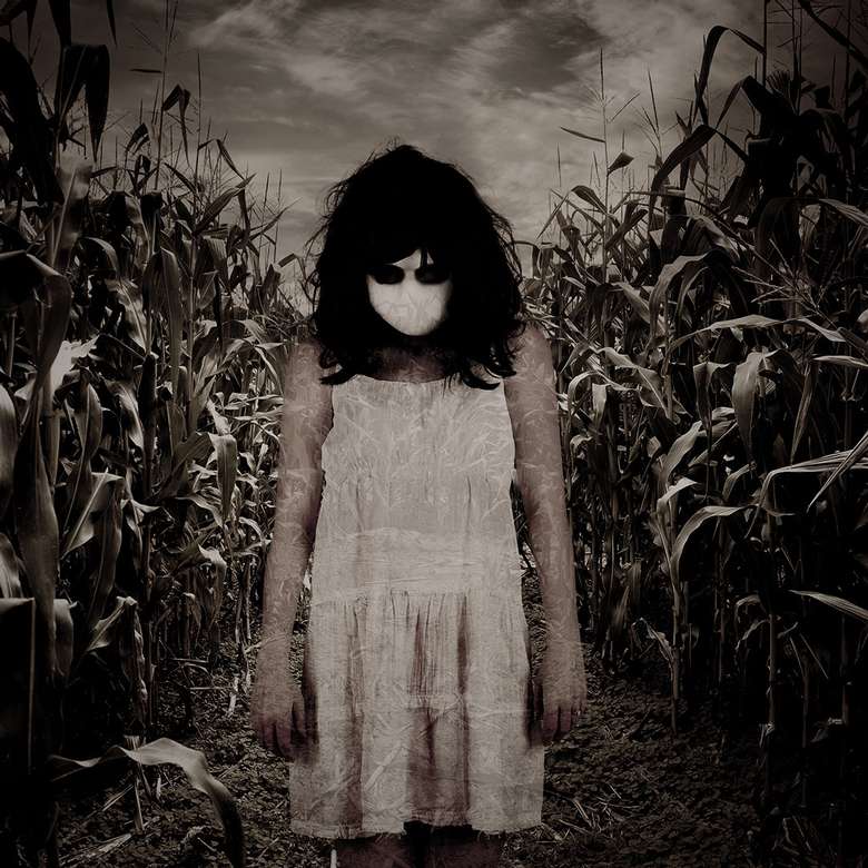 woman in dress and mask standing in creepy corn maze