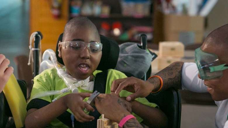 Boy in a wheelchair doing a craft with help from a male counselor