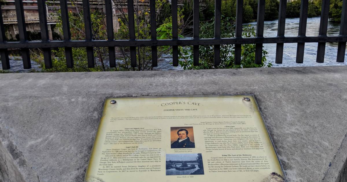 a sign at Cooper's Cave with a partial view of water
