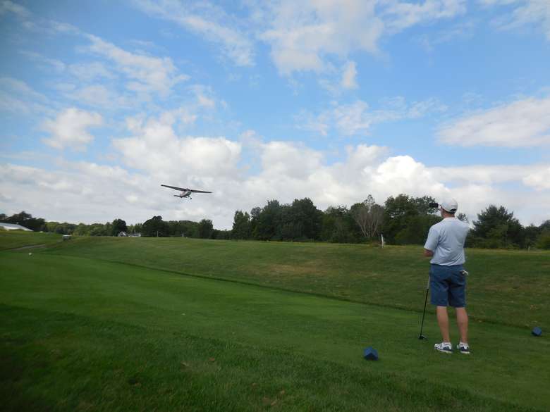 airplane taking off while a golfer looks on