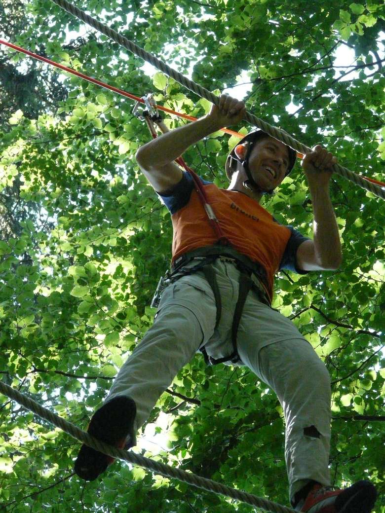 a man hanging between ropes on a treetop course