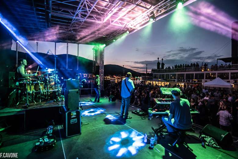 band performing for a crowd at night with a large steamboat in the background