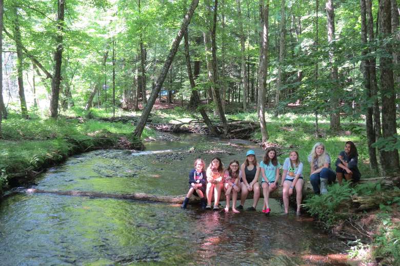 8 girls sit on a log over a creek