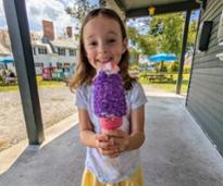 little girl holds up ice cream cone with purple sprinkles