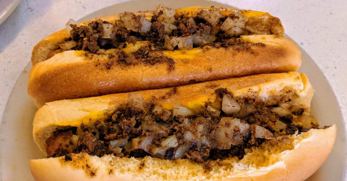 Close up of two hot dogs with onions and meat sauce on them