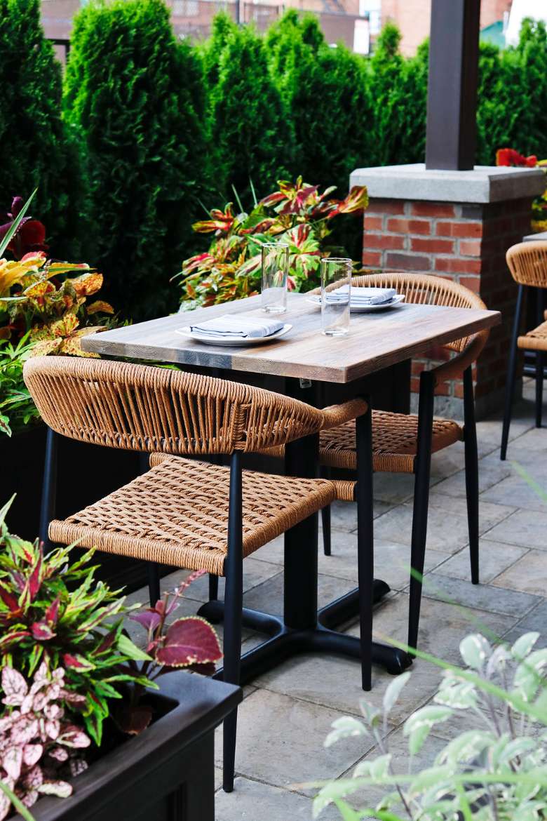 Enjoy happy hour or small plates on the heated patio. patio with table, two chairs, and hedges in the back.