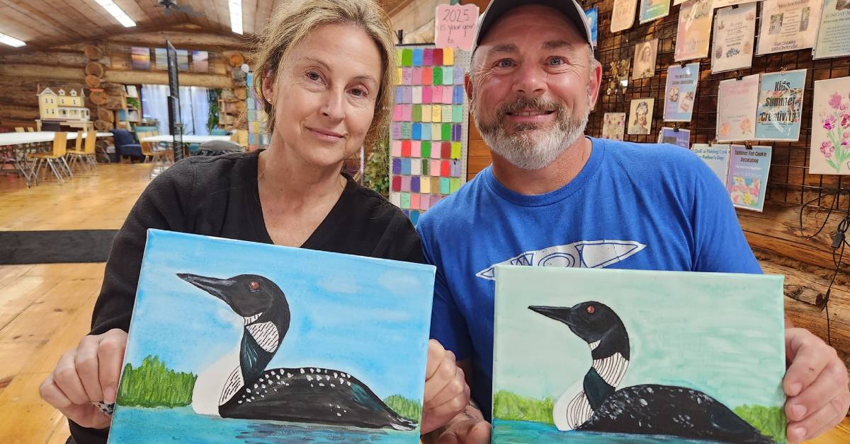two people holding up loon paintings