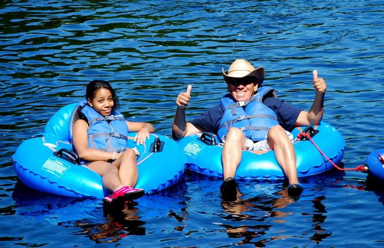 girl and a man sitting in separate blue tubes on a river, the man is giving a thumbs up