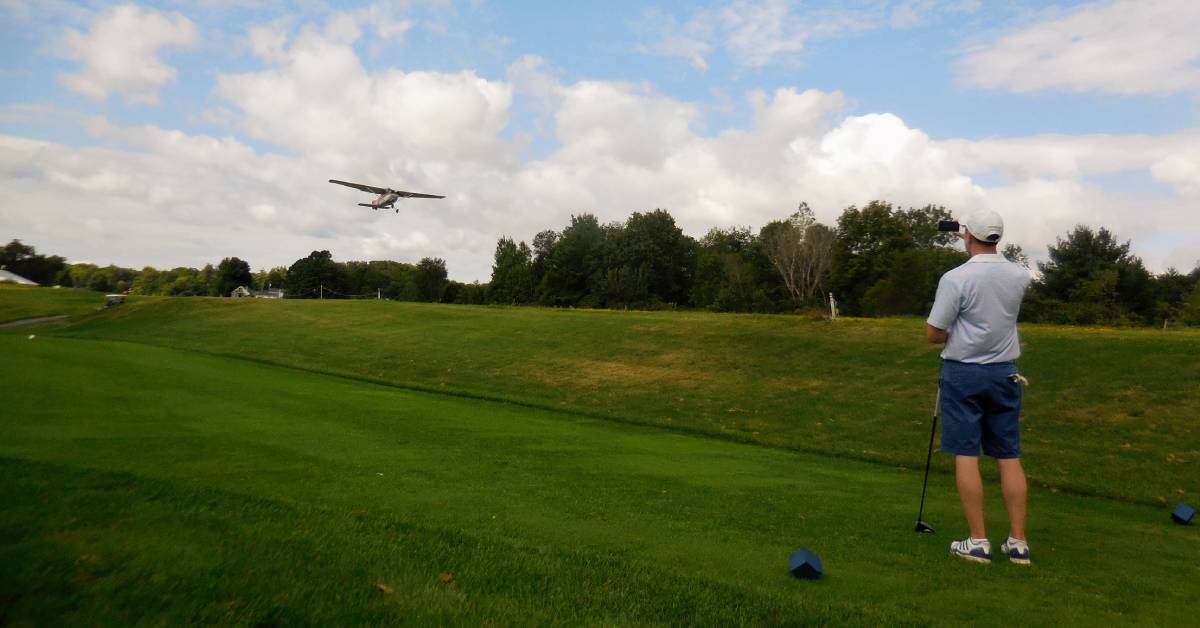 man takes photo of small airplane while on golf course