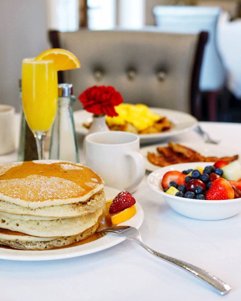 breakfast table with a stack of pancakes, a bowl of fruit, and a mimosa