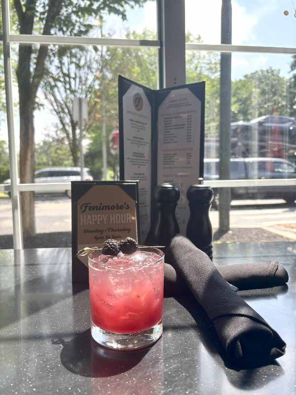 Cocktail in front of window and happy hour menu